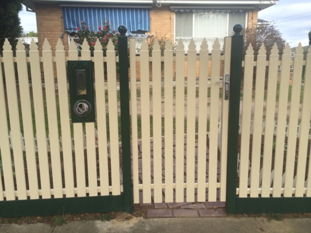 Cream steel picket fence with green letterbox, posts, and bottom rail